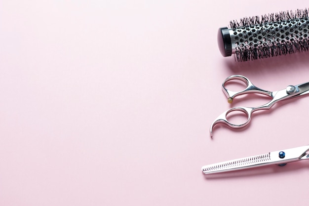 Scissors and comb on a pink background, copy space