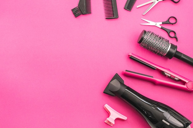 Scissors combs brushes hair dryer hair straightener and hairpin on a pink background