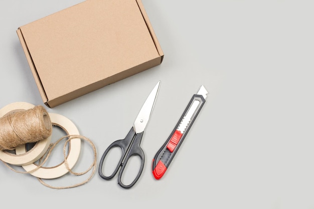 Scissors cutter masking tape and a cardboard box on a gray background in a top view