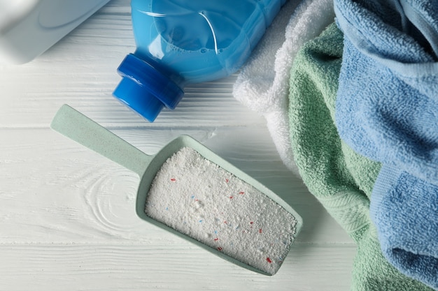 Scoop with powder, detergent and towels on white wooden table