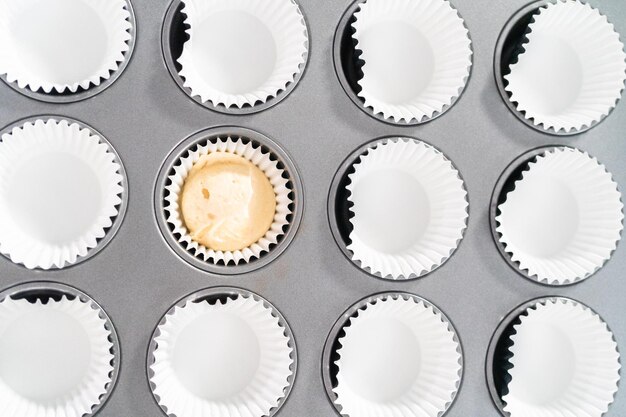 Scooping cupcake batter into cupcake pan lined with cupcake liners to bake vanilla cupcakes.