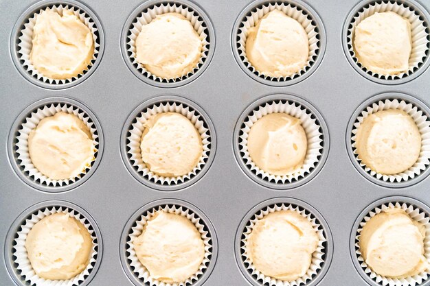 Scooping cupcake batter into cupcake pan lined with cupcake liners to bake vanilla cupcakes.