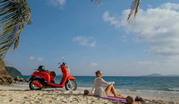 Scooter road trip Woman alone on red motorbike in white clothes on sand beach by ocean