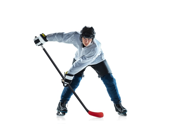 Scoring. Young male hockey player with the stick on ice court and white background. Sportsman wearing equipment and helmet practicing. Concept of sport, healthy lifestyle, motion, movement, action.