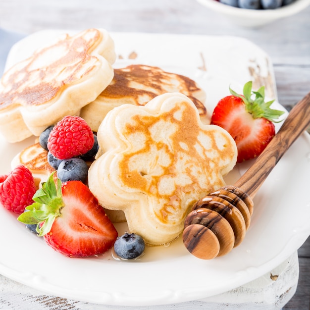 Scotch pancakes in flower form with berries and honey on white wooden background. 