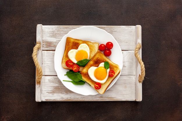 Scrambled eggs in the form of heart on plate with tomatoes, greens and coffee