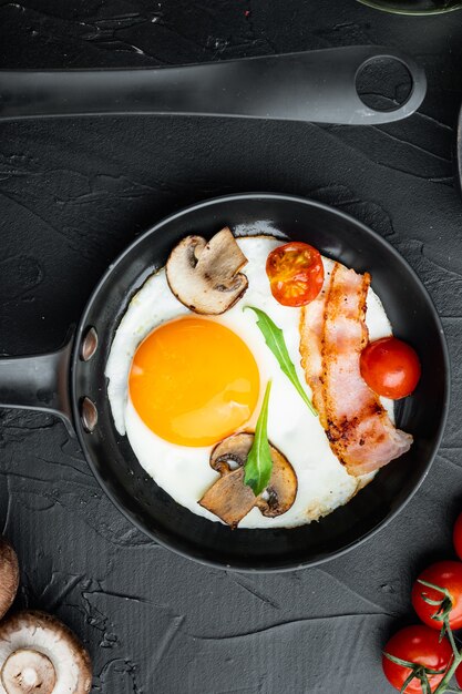 Photo scrambled eggs in frying pan with pork lard, bread and green feathers in cast iron frying pan, on black