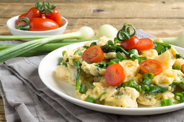 Scrambled eggs with spinach and tomatoes on a white plate.