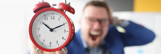 Screaming businessman holds red alarm clock in hands time management concept