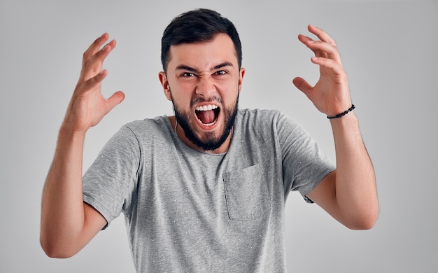 Screaming, hate, rage. Crying emotional angry man screaming on gray studio background. Emotional, young face. male half-length portrait. Human emotions, facial expression concept.