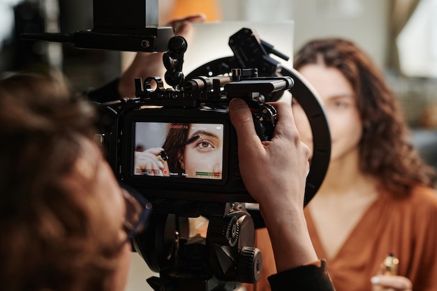 Screen of video camera with part of face of fashion model applying mascara