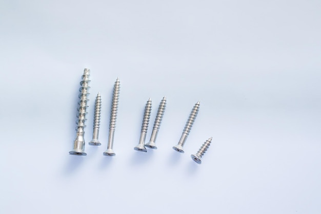 screw different sizes in a row on light blue background Stainless bolt Hardware repair tools