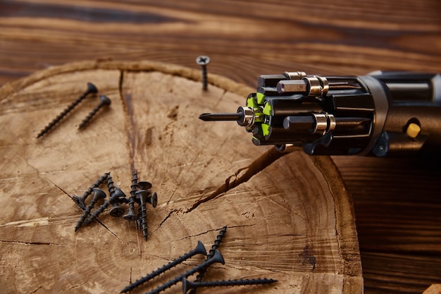 Screwdriver and self-tapping screws on stump, closeup, wooden table. Professional instrument, carpenter equipment, woodworker tools