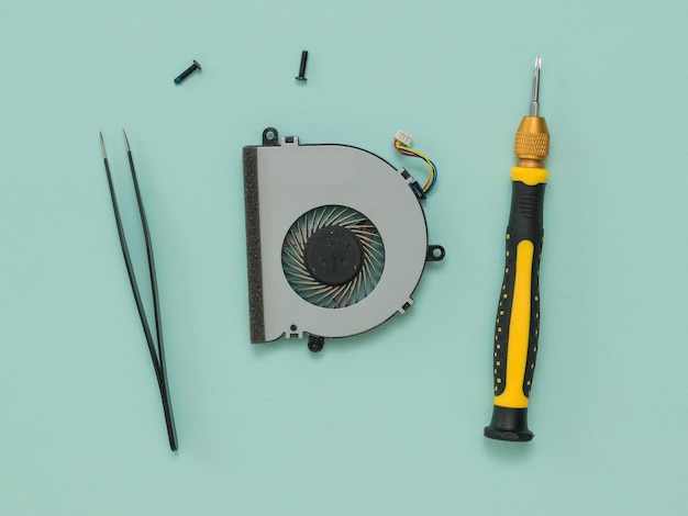 A screwdriver tweezers and a dismantled laptop cooling fan