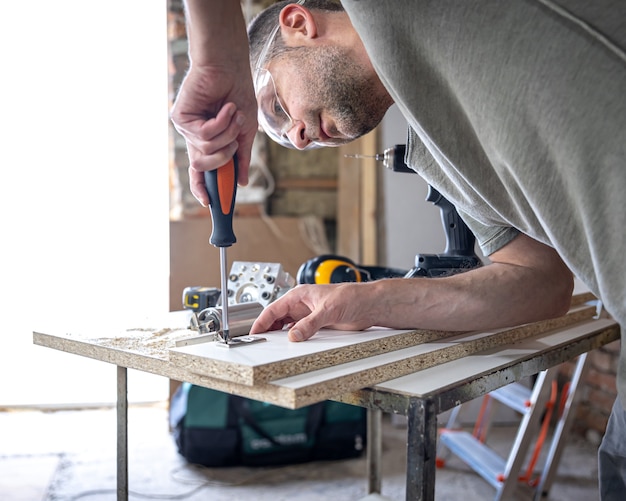 Screwing a self-tapping screw into a metal fastening hole on a wood strip using a screwdriver, the work of a carpenter.