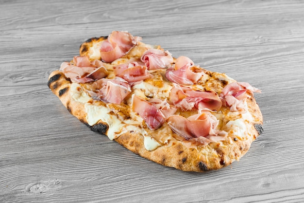 Scrocchiarella with pear, cheese, prosciutto on grey wooden background. Pinsa romana gourmet italian cuisine. Junk food.