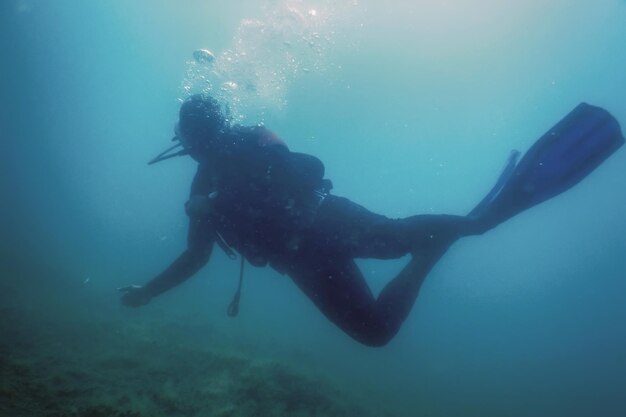 Scuba Diver Swimming Underwater Explores Reef and Examines Seabed