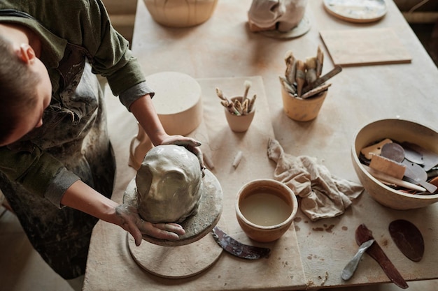 Sculptor using patterns and special equipment to make human face from clay in the workshop