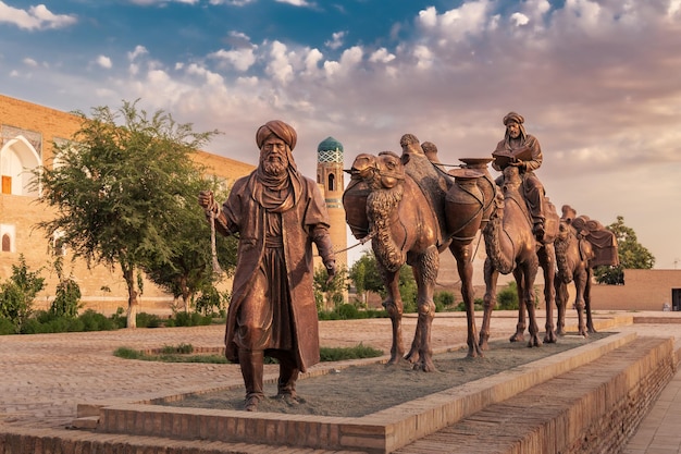 Sculpture of camel carrying goods and man in Uzbek dress in front of city walls Khiva Uzbekistan