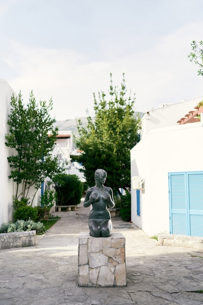 Sculpture of a seated naked girl on a pedestal in front of buildings