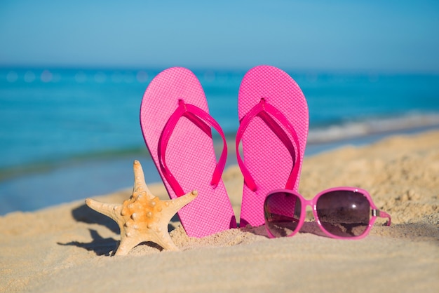 The sea, beach, sand and women's accessories: pink flip-flops, sunglasses and starfish