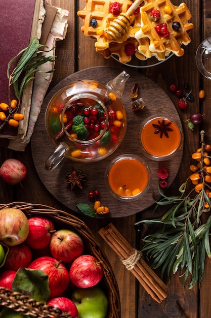 Sea buckthorn and raspberries in a glass teapot cups with poured tea Apples and waffles with honey