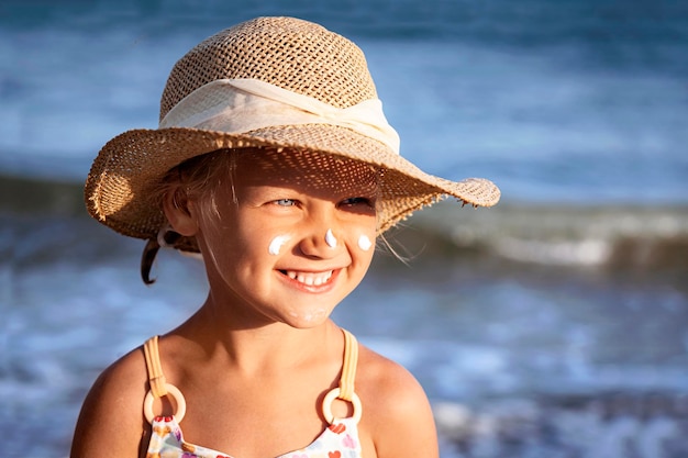 Sea Children Holiday. Happy Sea Child Little Girl with Sunscreen Protection on Face on Sea Beach.