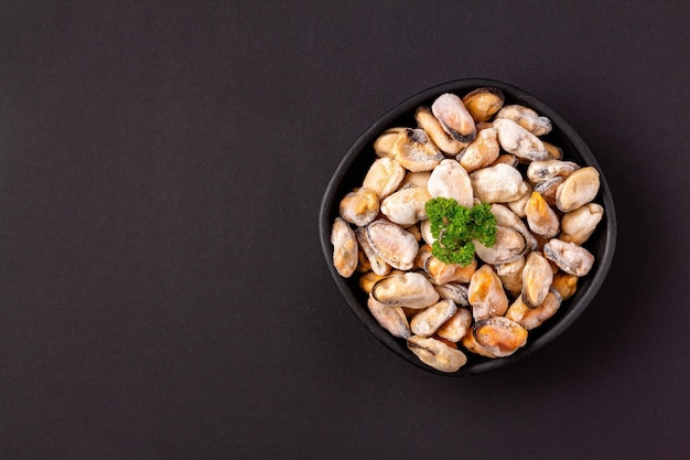 Sea clams meat with green parsley in a dish on a black background with copy space, flat lay.