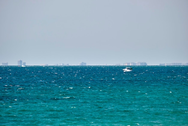 Sea panorama Small motor boat floats in deap blue bay water under bright blue sky tall buildings on distant shore