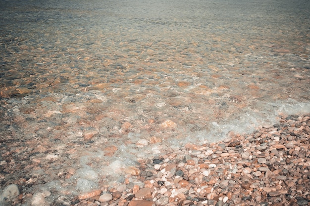 Sea pebbles and stones underwater textural seabed through clear transparent blue water natural backg...