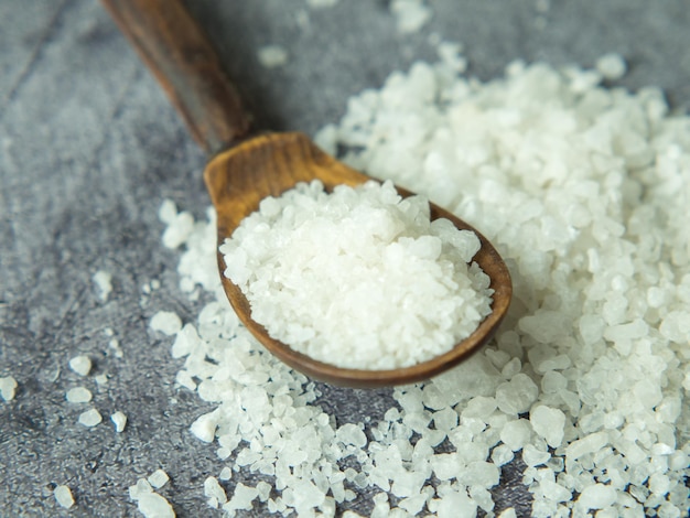 Sea salt a pile of sea salt in a wooden spoon on a dark stone background closeup