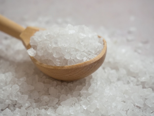 Sea salt, a pile of sea salt in a wooden spoon on a light concrete background