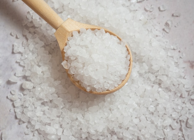 Sea salt, a pile of sea salt in a wooden spoon on a light concrete background