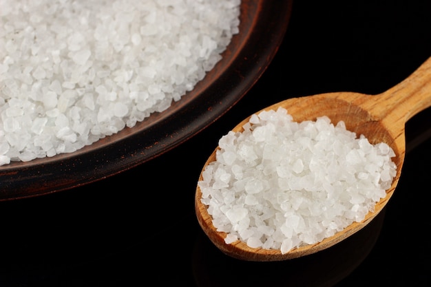 Sea salt in a plate and a spoon on a black surface