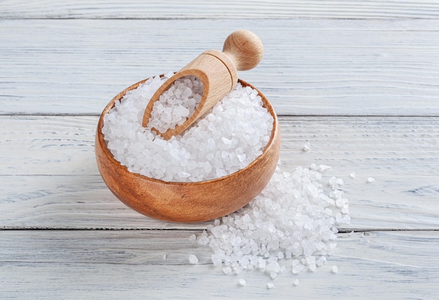 Sea salt in wooden bowl with scoop on white wooden background