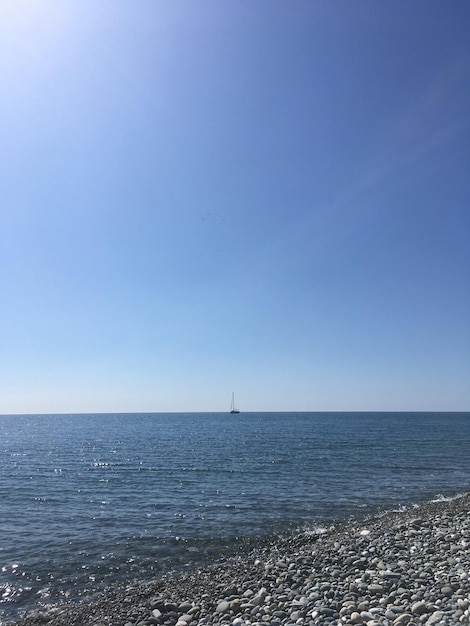 Sea. Stone beach and blue sky without clouds. The ship is far on the horizon. Mobile photography.