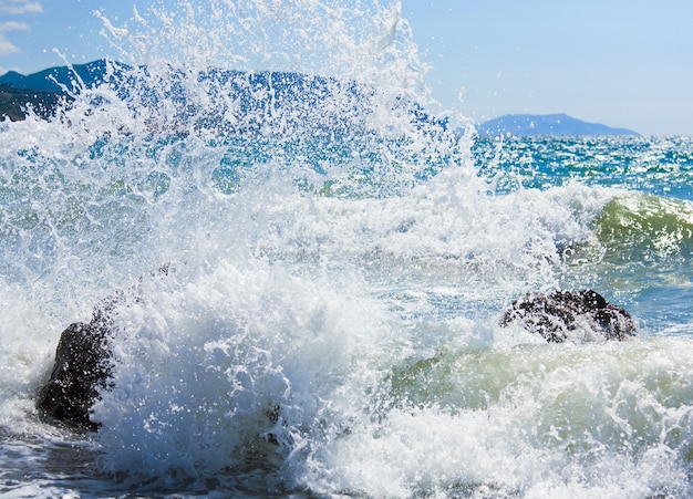 Sea surf wave break on coastline and Meganom cape on horizon right