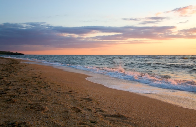 Sea surf wave break on sunset sandy coastline