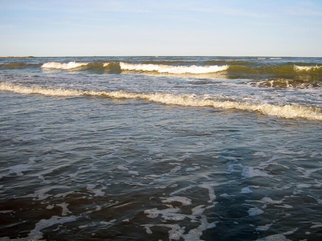 Sea waves are rolling onto the beach of an empty summer beach covered with small stones