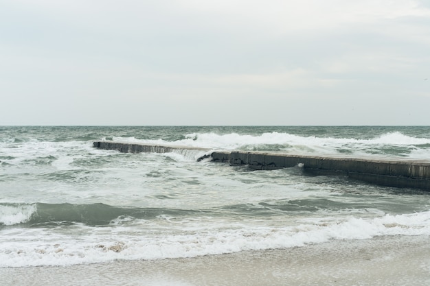 Sea waves breaking on the concrete breakwater cloudy day