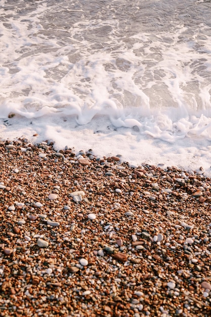 Sea waves run on orange pebbles on the beach