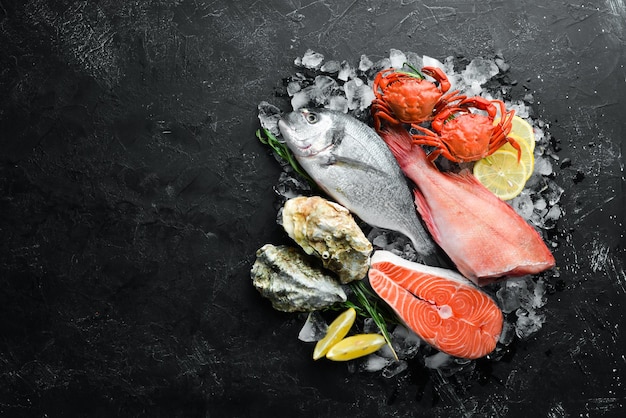 Seafood: Dorado, salmon, crab, grouper, oysters. On a black stone background. Top view. Free space for your text.