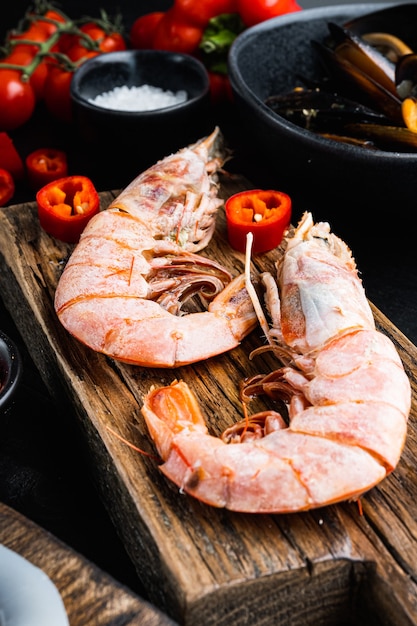 Seafood king prawns on wooden board with spices over black wood table, food photo.