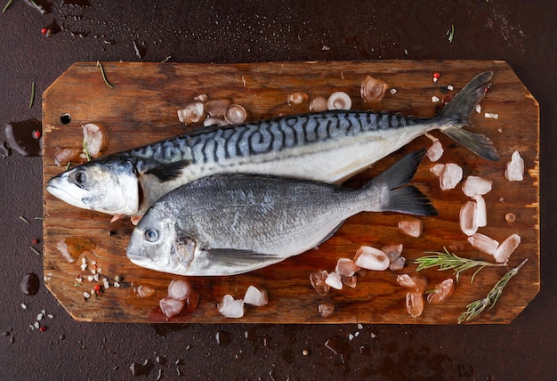 Seafood restaurant background. Fresh mackerel and dorado fish on wooden board on brown table. Organic cooking ingredients for healthy food. Top view, copy space