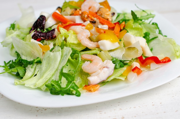 Seafood salad with vegetables and lettuce on white plate