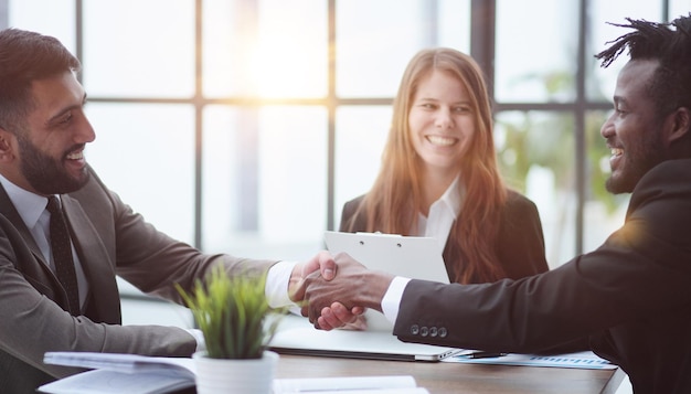 Sealing a deal Business people shaking hands while sitting at the desk in office