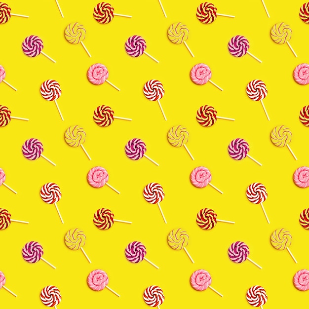 Seamless pattern with sweet round candy lollypops with stripes on stick on yellow paper background.