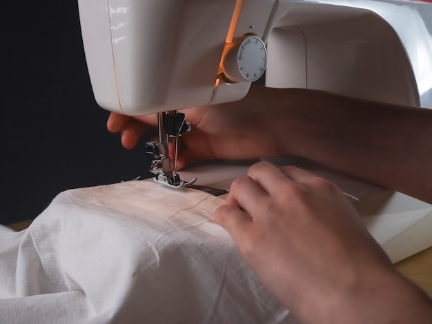 Seamstress hands with cloth at sewing machine during work.