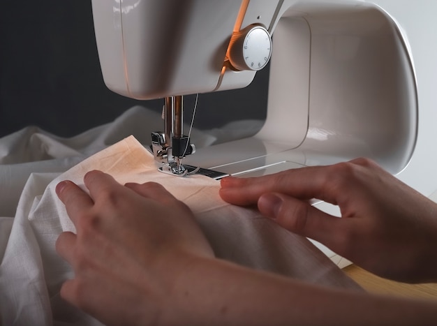 Seamstress hands with cloth at sewing machine during work