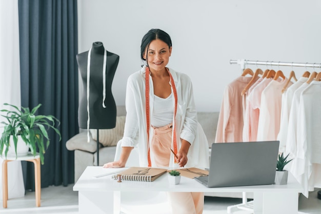 Seamstress is standing in her office that is with different clothes